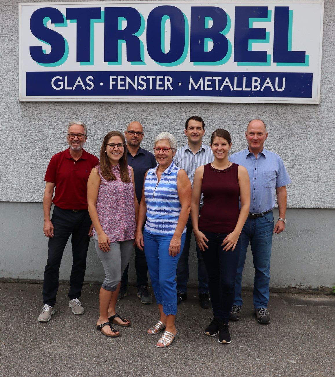 Das Team der Strobel GmbH vor dem Firmenschild „Glas · Fenster · Metallbau“